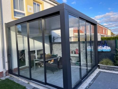 Geschlossener Anbau aus anthrazitfarbenen Aluminiumprofilen mit umlaufenden Glasschiebeelementen an einem Wohnhaus